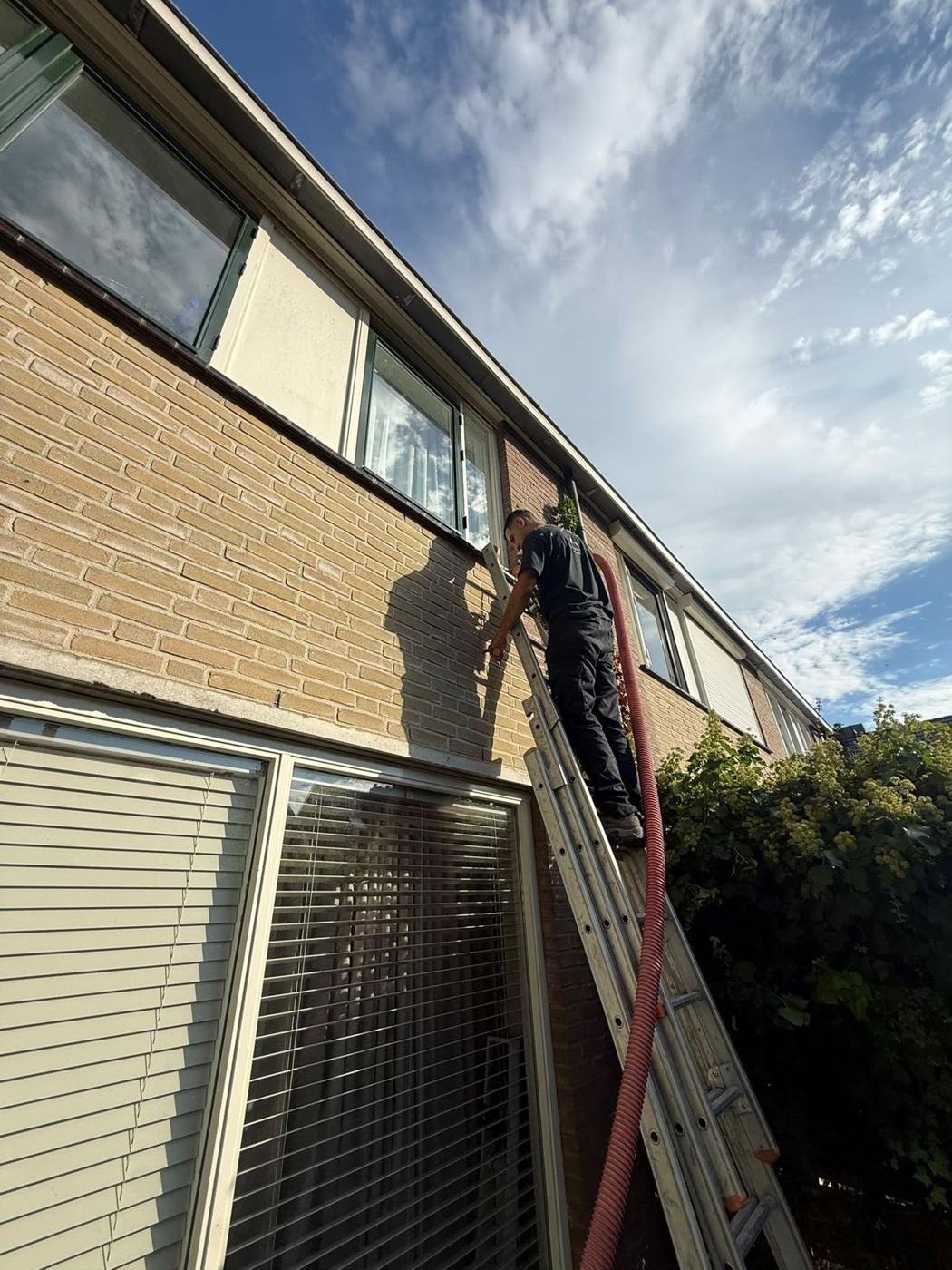 Vakman op een ladder vult de spouwmuur van een rijtjeswoning met isolatie