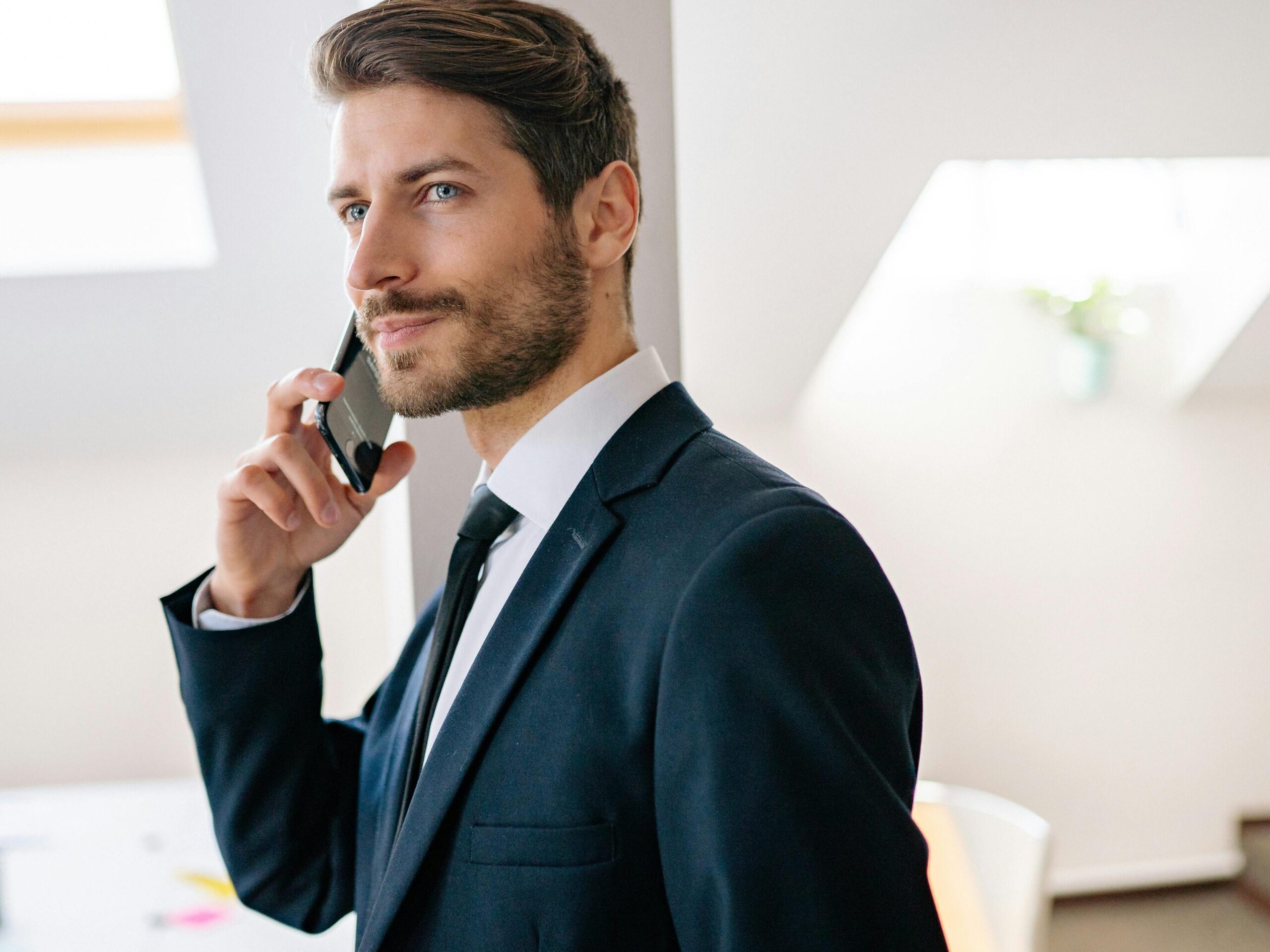 Professional businessman in a suit making a phone call in a modern office setting.